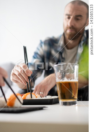 Man eating sushi with chopsticks Man eating sushi with chopsticks 141085133