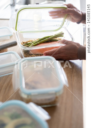 Woman opening a healthy salmon meal prep container in the kitchen Woman opening a healthy salmon meal prep container in the kitchen 141085145