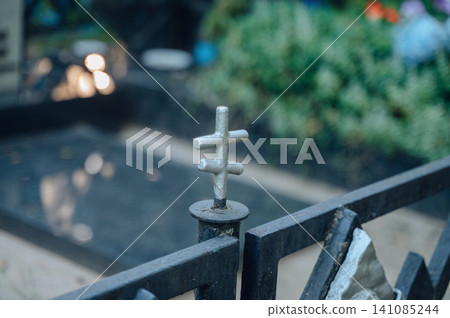Close-up view of a small four-pointed metal cross decoration atop a decorative wrought iron cemetery fence Close-up view of a small four-pointed metal cross decoration atop a decorative wrought iron cemetery fence 141085244