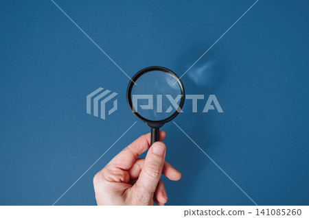 Hand holding a classic magnifying glass against a blue background with copy space, search and discovery concept Hand holding a classic magnifying glass against a blue background with copy space, search and discovery concept 141085260