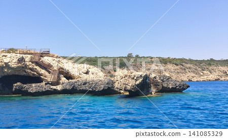 Rocky coastline of Protaras, Cyprus with crystal clear Mediterranean Sea, sea cave, and coastal stairs viewed from a boat on a sunny summer day. Perfect travel and vacation destination Rocky coastline of Protaras, Cyprus with crystal clear Mediterranean Sea, sea cave, and coastal stairs viewed from a boat on a sunny summer day. Perfect travel and vacation destination 141085329