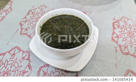 Molokhia and shrimp soup in a white bowl placed on a tablecloth  141085414