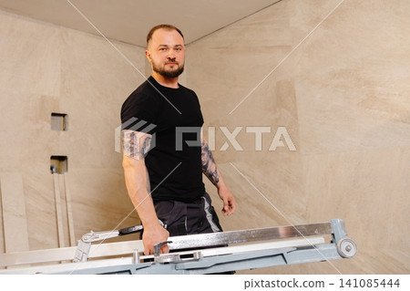 Tiler carrying tile cutter in bathroom during renovation Tiler carrying tile cutter in bathroom during renovation 141085444