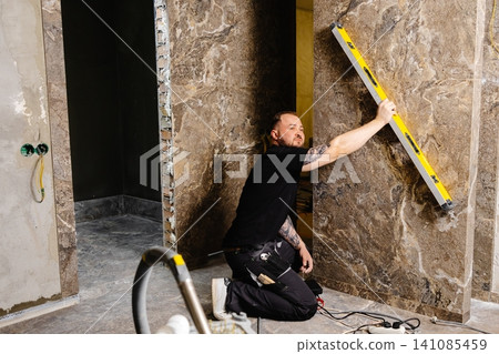 Construction worker using spirit level installing marble tile on wall Construction worker using spirit level installing marble tile on wall 141085459
