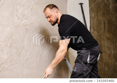 Construction worker vacuuming dust and debris after laying tiles in bathroom Construction worker vacuuming dust and debris after laying tiles in bathroom 141085460