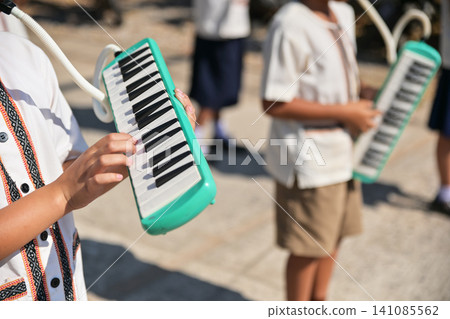 Close-up of a student playing a green melodica in a school marching band outdoors. Close-up of a student playing a green melodica in a school marching band outdoors. 141085562