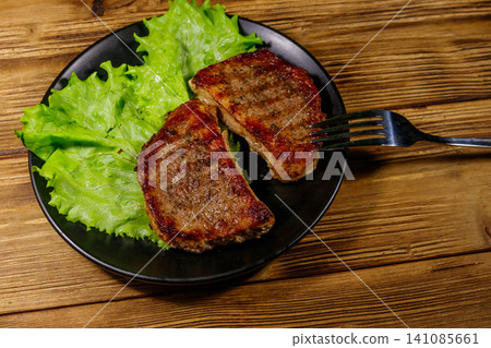 Grilled pork steaks with lettuce leaves on wooden table Grilled pork steaks with lettuce leaves on wooden table 141085661