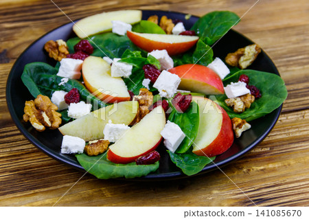 Autumn spinach salad with apple, feta cheese, walnut and dried cranberry on wooden table. Healthy vegetarian food Autumn spinach salad with apple, feta cheese, walnut and dried cranberry on wooden table. Healthy vegetarian food 141085670