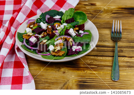 Tasty spinach salad with boiled beetroot, feta cheese, walnut and red onion on wooden table. Healthy vegetarian food Tasty spinach salad with boiled beetroot, feta cheese, walnut and red onion on wooden table. Healthy vegetarian food 141085673