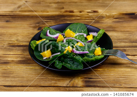 Tasty salad with spinach, orange, red onion and sesame seeds on wooden table. Healthy food or vegetarian concept Tasty salad with spinach, orange, red onion and sesame seeds on wooden table. Healthy food or vegetarian concept 141085674