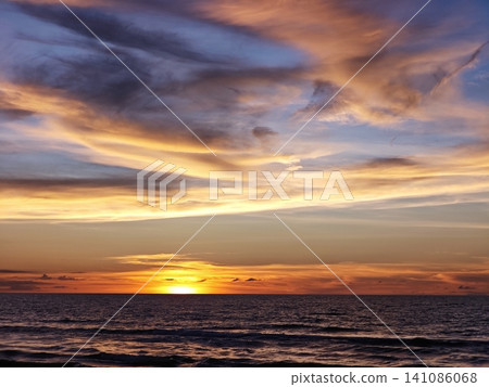 Vibrant sunset sky with dramatic clouds over a tranquil ocean horizon Vibrant sunset sky with dramatic clouds over a tranquil ocean horizon 141086068