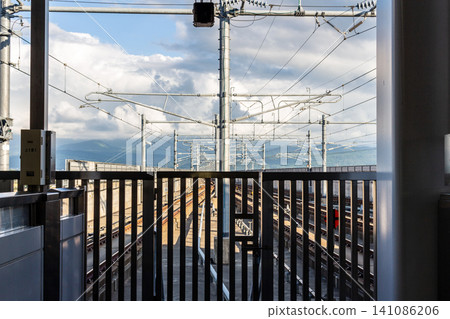 The Shinkansen tracks and complex overhead wires, the blue sky with clouds and mountain ranges, the view from beyond the fence of the station platform. The Shinkansen tracks and complex overhead wires, the blue sky with clouds and mountain ranges, the view from beyond the fence of the station platform. 141086206