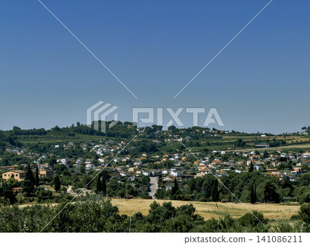 Panoramic view of a small town nestled in green hills under blue sky. Panoramic view of a small town nestled in green hills under blue sky. 141086211