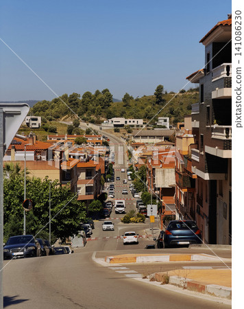 City street with cars and orange roof houses under blue sky. City street with cars and orange roof houses under blue sky. 141086230
