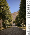 Cobblestone Path Lined with Green Trees Leading to a Building 141086300