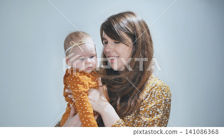 Loving mother tenderly embracing newborn daughter, sharing warm connection against soft blue backdrop 141086368