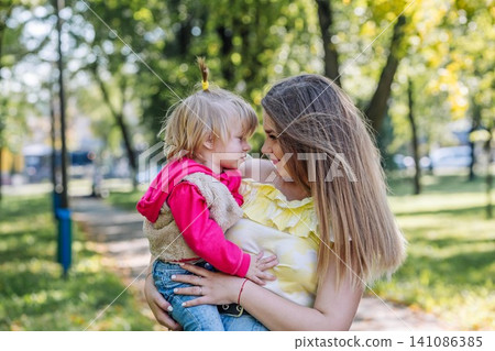 Mother hugging daughter while sitting on park bench, enjoying warm sunlight and close family connection Mother hugging daughter while sitting on park bench, enjoying warm sunlight and close family connection 141086385