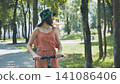 Young woman enjoying a sunny day riding an electric scooter in a green park, embracing sustainable transportation and outdoor leisure 141086406
