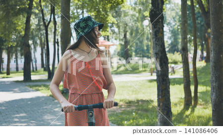 Young woman enjoying a sunny day riding an electric scooter in a green park, embracing sustainable transportation and outdoor leisure Young woman enjoying a sunny day riding an electric scooter in a green park, embracing sustainable transportation and outdoor leisure 141086406