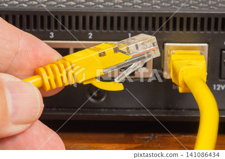 Hand plugging a yellow ethernet cable into a network router port, close-up. Hand plugging a yellow ethernet cable into a network router port, close-up. 141086434