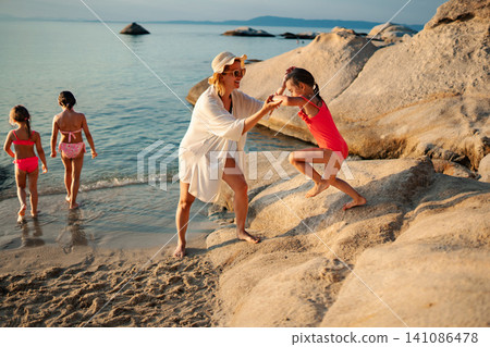 Mother helping child climb rocks on summer beach vacation 141086478