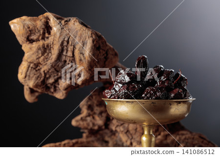 Spicy dried black olives in a vintage brass bowl on a background of weathered olive tree snags. Spicy dried black olives in a vintage brass bowl on a background of weathered olive tree snags. 141086512