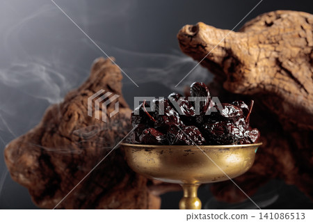 Dry cured black olives in a vintage brass bowl on a background of weathered olive tree snags. Dry cured black olives in a vintage brass bowl on a background of weathered olive tree snags. 141086513