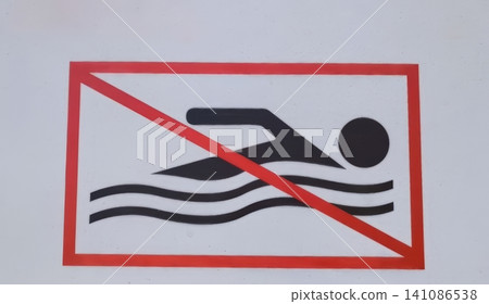 White sign with red border and diagonal line crossing a black silhouette of a swimmer in water, indicating swimming is prohibited. 141086538