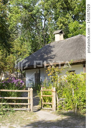 Rural peasant house surrounded by blooming flowers and trees in a serene countryside setting 141087029