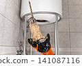 Plumber Holding Removed Water Heater Heating Element Covered With Heavy Mineral Deposits, Showing Hard Water Damage And Maintenance Service Process 141087116