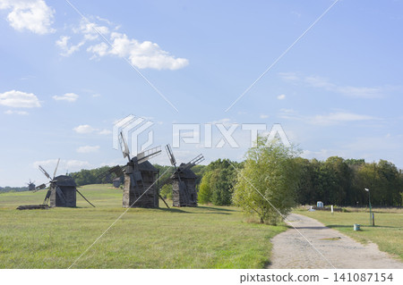Rural dirt road leading past old windmills under clear sky in tranquil landscape Rural dirt road leading past old windmills under clear sky in tranquil landscape 141087154