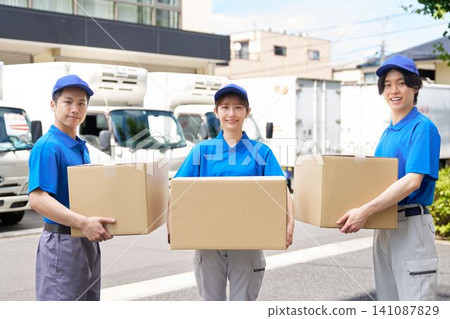 A delivery staff member smiles while holding cardboard boxes, with a truck in the background. A delivery staff member smiles while holding cardboard boxes, with a truck in the background. 141087829
