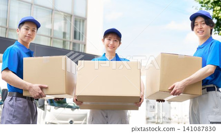 A delivery staff member smiles while holding a cardboard box. A delivery staff member smiles while holding a cardboard box. 141087830