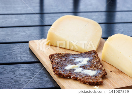 Sourdough wholegrain rye bread  with melting butter, served with cheese on a wooden board. 141087859