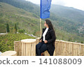Young Indian woman sitting at a bamboo cafe overlooking the scenic tea gardens of Tinchuley in Darjeeling 141088009