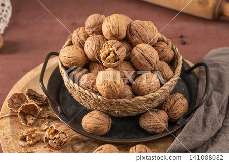 A high-angle commercial shot of fresh whole walnuts piled in a woven basket atop a rustic metal tray and wooden board with earthy tones and soft lighting for a natural organic food aesthetic 141088082