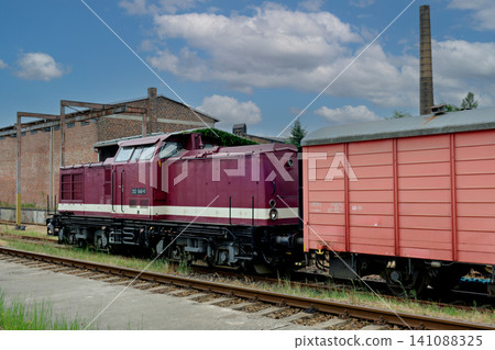 Vintage maroon diesel locomotive coupled to a red freight wagon Vintage maroon diesel locomotive coupled to a red freight wagon 141088325