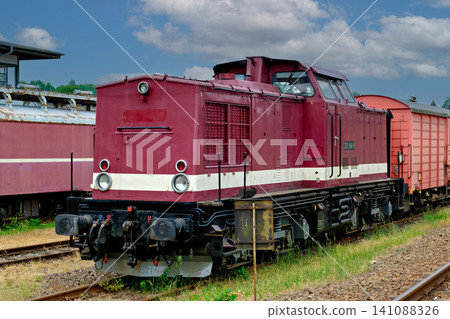 Vintage burgundy diesel locomotive parked on a railway track under a cloudy blue sky Vintage burgundy diesel locomotive parked on a railway track under a cloudy blue sky 141088326