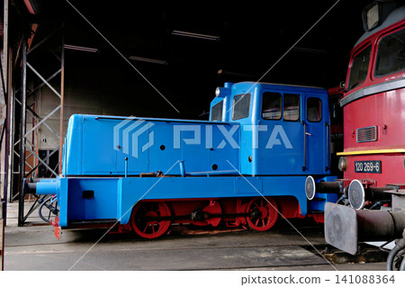 Vintage blue industrial shunting locomotive with red wheels inside a dark depot hangar Vintage blue industrial shunting locomotive with red wheels inside a dark depot hangar 141088364