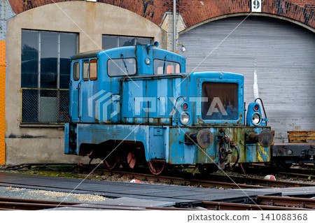 Old blue industrial shunting diesel locomotive parked outside historic brick train depot station Old blue industrial shunting diesel locomotive parked outside historic brick train depot station 141088368