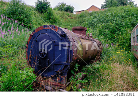 Discarded old steam train boiler sitting in a field of wild flowers Discarded old steam train boiler sitting in a field of wild flowers 141088391