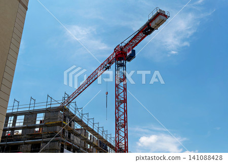 Large red industrial construction crane building a new house under blue sky Large red industrial construction crane building a new house under blue sky 141088428