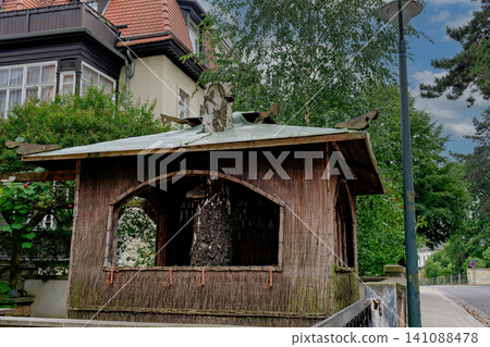 Small rustic wooden decorative hut built around a birch tree trunk in a public park Small rustic wooden decorative hut built around a birch tree trunk in a public park 141088478