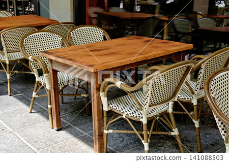 Empty wooden table and wicker bistro chairs at an outdoor cafe terrace 141088503