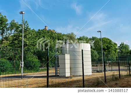 Industrial utility facility with white tank and distant historic castle ruin on hill Industrial utility facility with white tank and distant historic castle ruin on hill 141088517