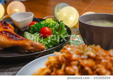The table features a blurred pasta in the foreground and a focused roast chicken and salad in the background. 141089204