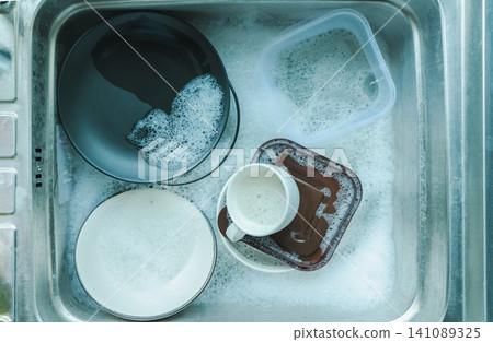 top view of plates and crockery, coffee mugs in the sink employing dishes with sponge and bubbles of dishwashing liquid, washing and cleaning chores concepts top view of plates and crockery, coffee mugs in the sink employing dishes with sponge and bubbles of dishwashing liquid, washing and cleaning chores concepts 141089325