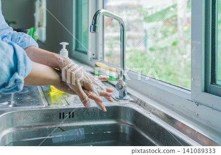 Asian hand woman wearing blue shirt washing both hands. clean your finger with water and foam soap in the kitchen sink before eating. concept germ safety Asian hand woman wearing blue shirt washing both hands. clean your finger with water and foam soap in the kitchen sink before eating. concept germ safety 141089333