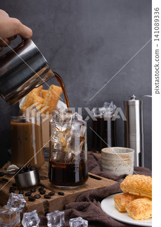 Pour milk make latte coffee, Asian iced coffee in transparent glass and roasted coffee beans and Crispy Pie on wood. black background studio photo, Copy space for your text 141089336