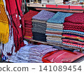 Stacks of colorful traditional ethnic woven fabrics and handmade textiles on display at a local market. Great for asian culture, travel souvenir, and fashion textile concepts. 141089454